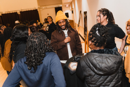 A small group of students gather around a visiting musical artists for a meet and greet.