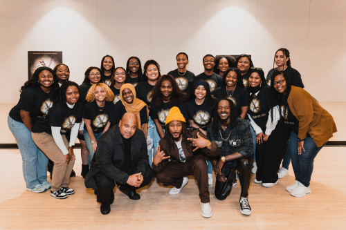 Students pose in a large group behind visiting musical artists.