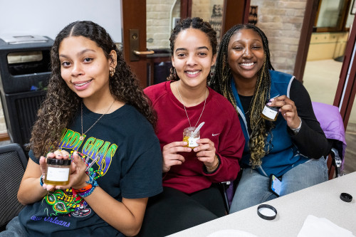 Three students sit at a table and pose with their homemade hair care products.