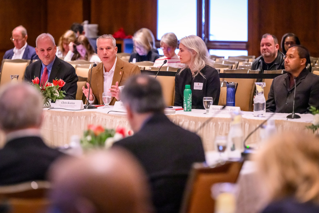 People in business attire sit at a long table with name plates in front of them. They're part of a panel discussion on public private partnerships in Wisconsin.