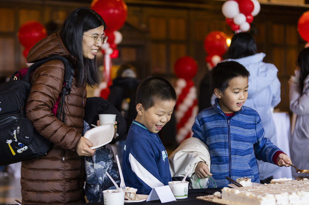 Two children and a woman pick up ice cream and cake at a table, all smiling in excitement.