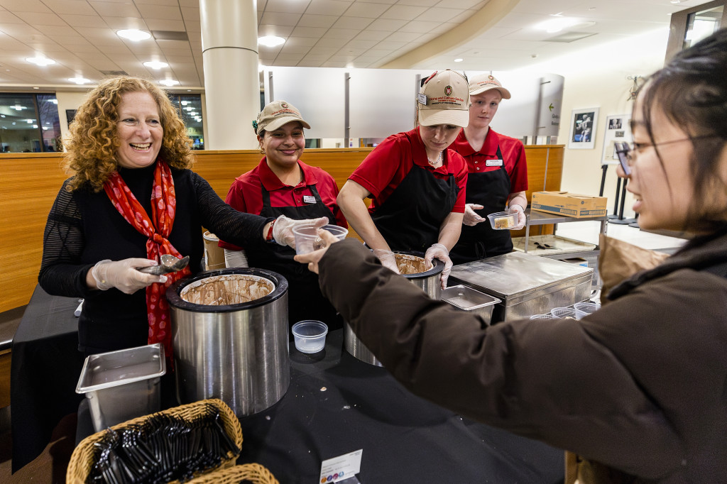 A woman scoops ice cream, a person on the other side of the table receives it with a smile.