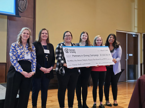 Six people stand in a row, smiling and holding a large ceremonial check made out for $1,934,302.98.