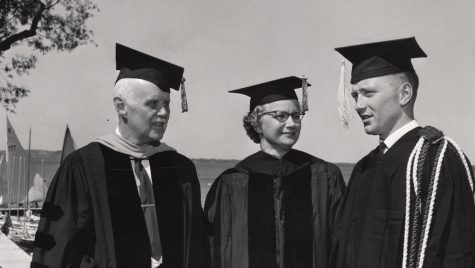 Three people, two men and one woman, talk outdoors while dressed in academic regalia.