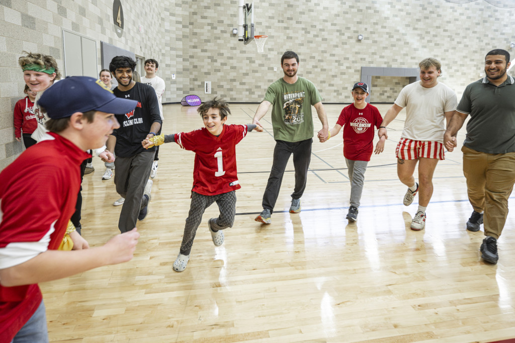 Middle school students and college students smile as they play a game on the basketball court.