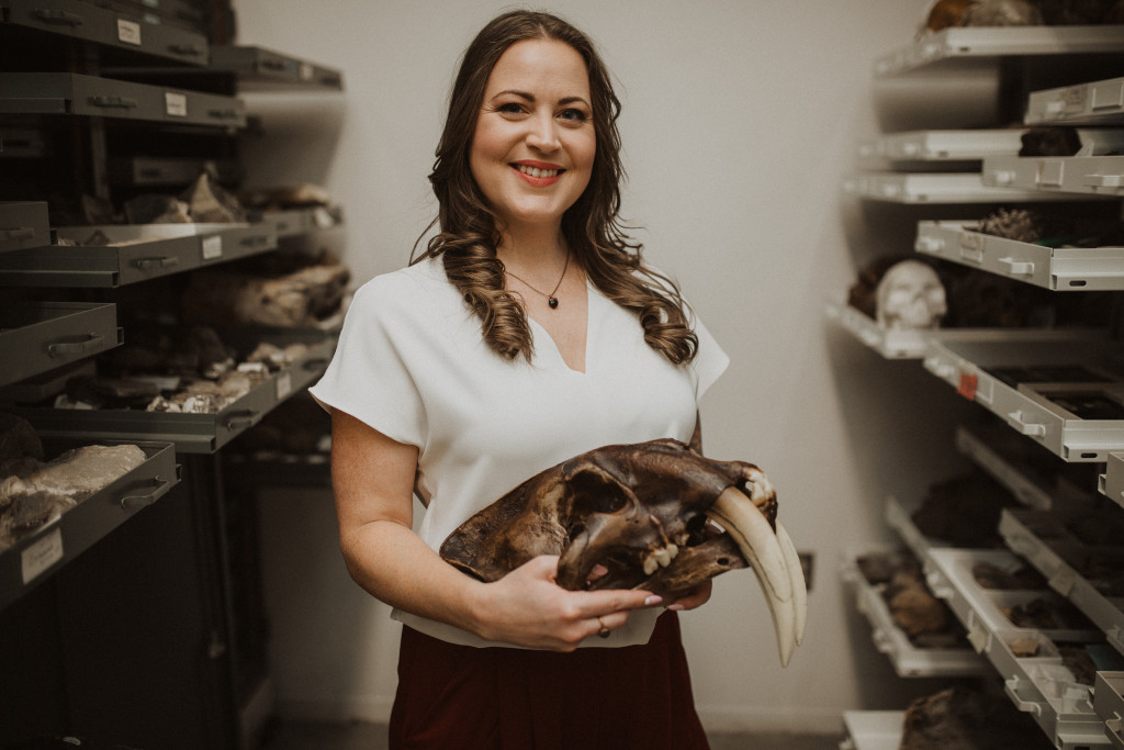 A woman holds the skull of a prehistoric cat.