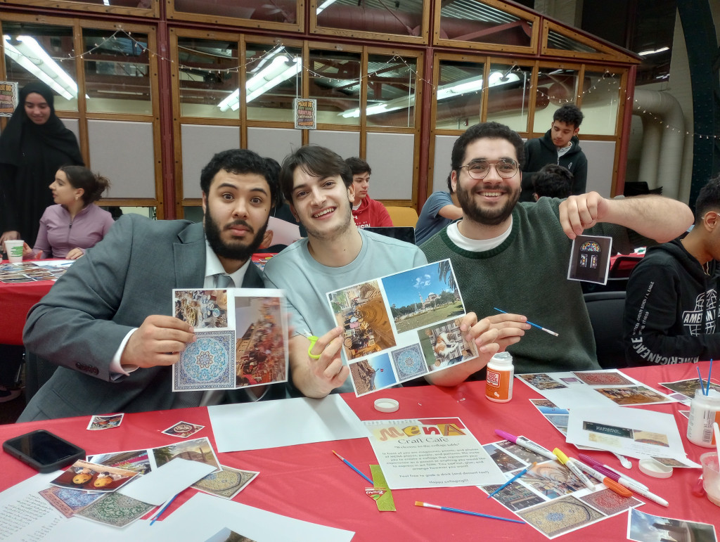 Three students sit at a table and pose with their crafts