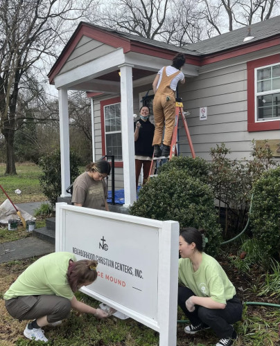 People fix up a sign in front of a building.