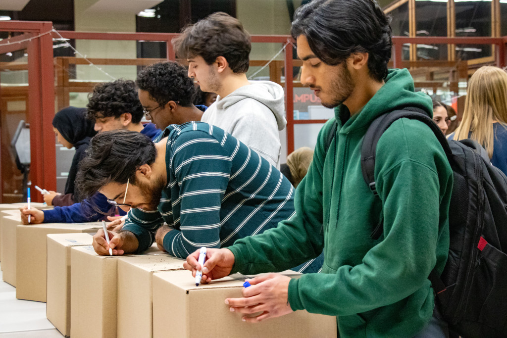 People stand in line at a table labeling boxes of food and other goods.