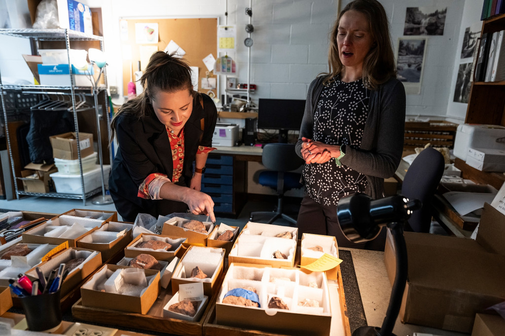 Two women inspect rocks on a desk.