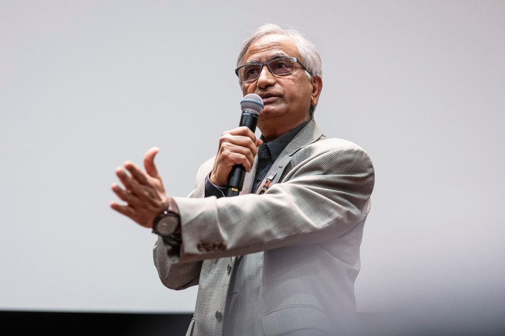 Masood Akhtar stands and speaks into a microphone.