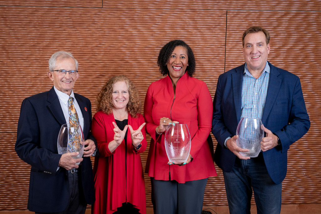 Four people pose for the camera, three of them holding trophies.