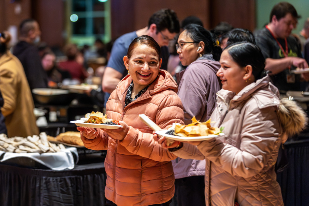 People holding plates of food stand and talk while eating.