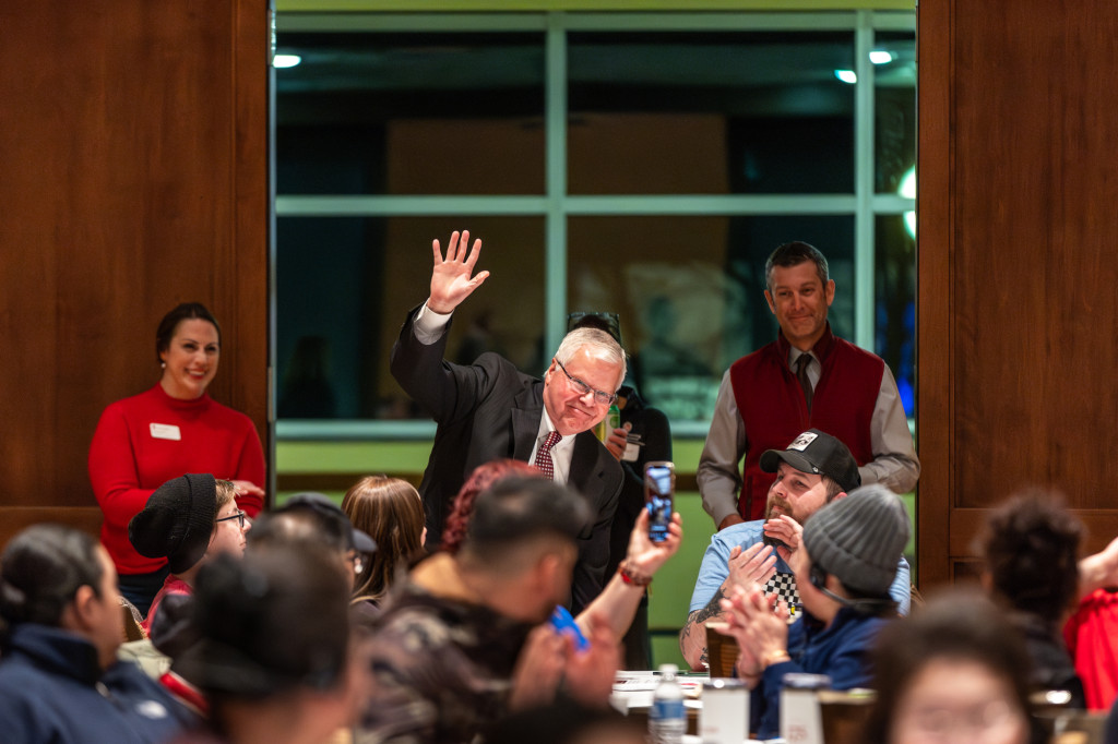 A man sitting at a table waves to the crowd.