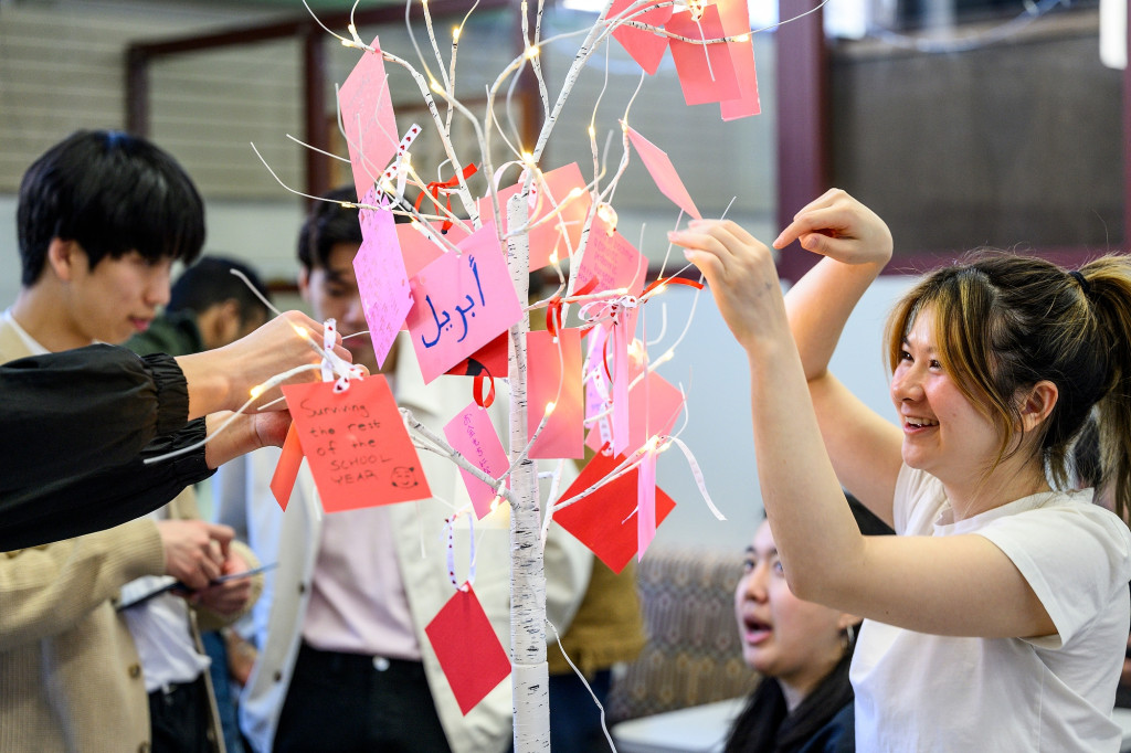 A woman hangs a paper ornament on a tree.