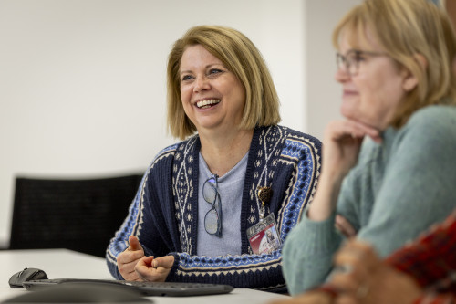 Barbara Anderson smiles as she sits at a table interacting with colleagues.