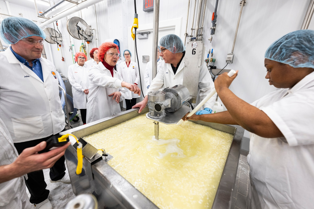 Several people stand around a vat of yellow liquid and talk.