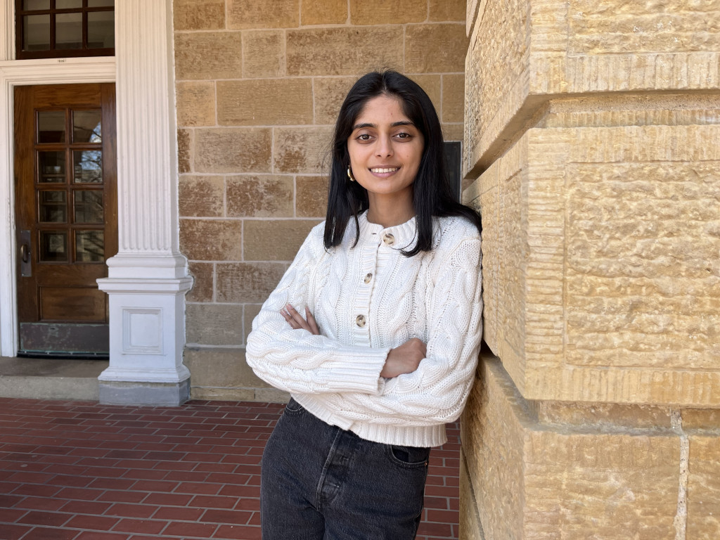 A woman smiles at the camera and leans against a wall.