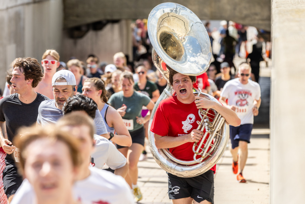 A man holding a Tuba runs and smiles.