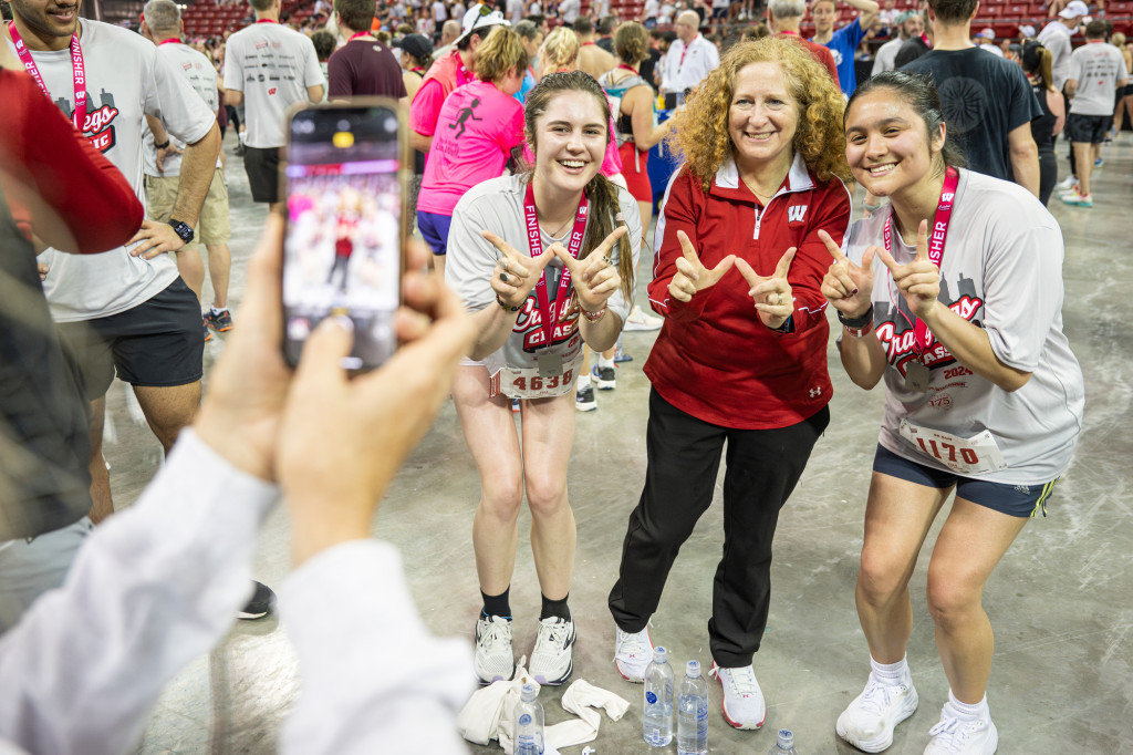 Three women smile and pose for a photo together, flashing the W symbol with their hands.