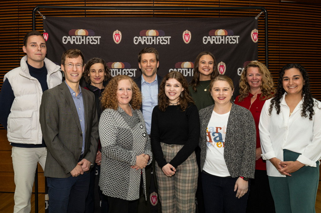 A group of people smile and look at the camera, standing in front of a backdrop with the UW–Madison Earth Fest logo.