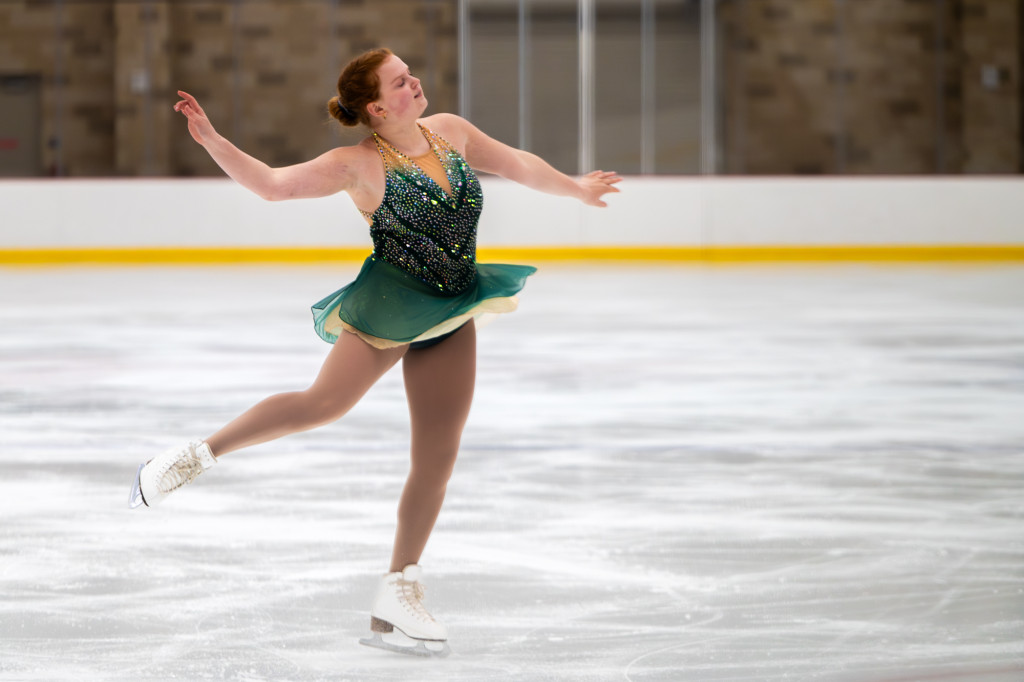 A woman in a green dress skates on an ice rink.