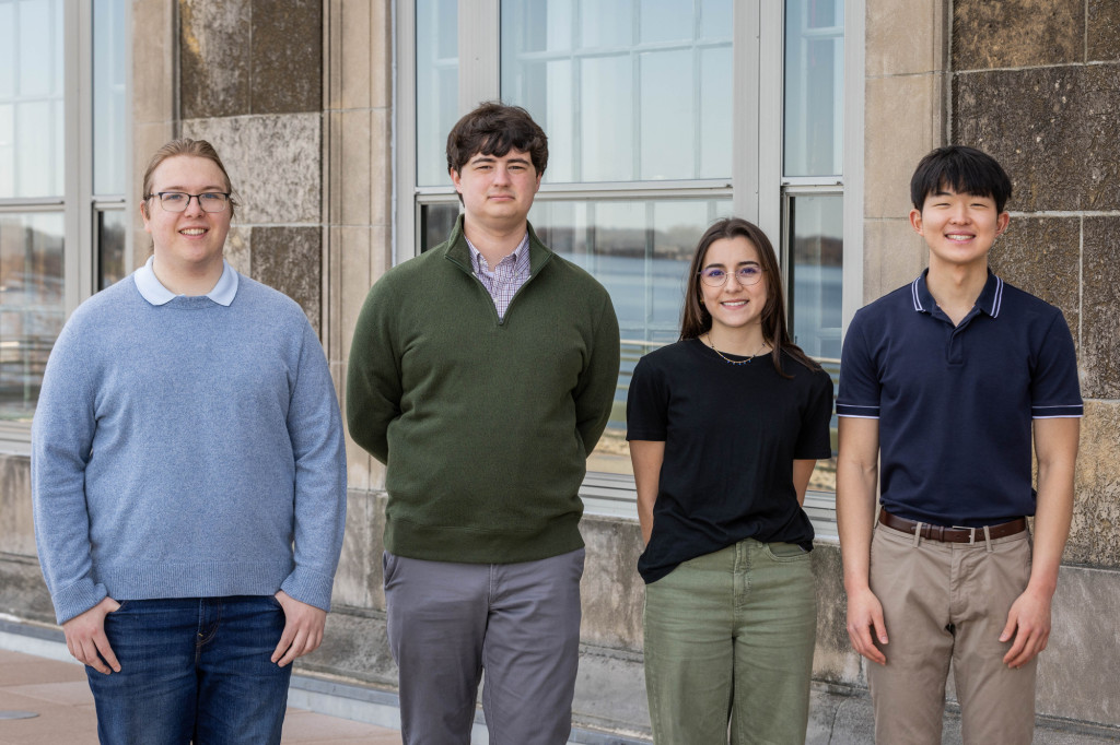 Four students stand in a row and smile to the camera.