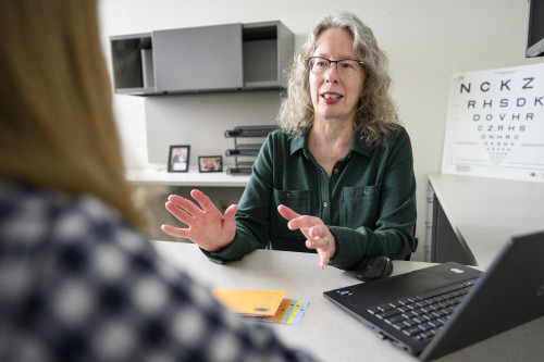 Photo of Carla Schubert seated at a table and speaking with a student