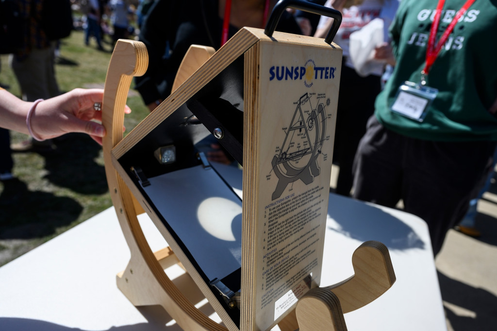 A person uses a machine to show the eclipsed sun's crescent-shaped shadow.