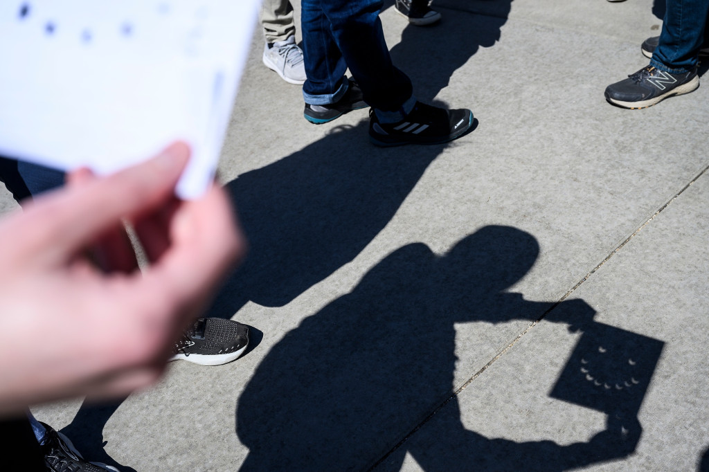 Undergraduate student Sam Rosenman holds a sheet of paper in the sun with holes pouched to make a smiley face of crescent shadows during the eclipse.