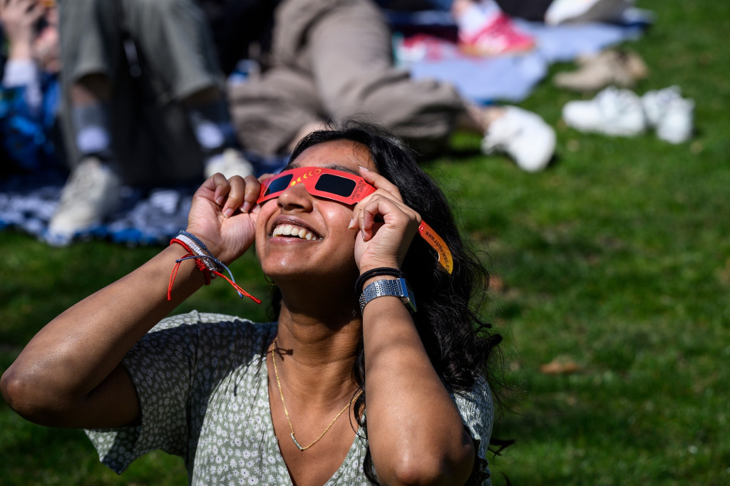 A woman wearing special glasses looks up to the sun, smiling.