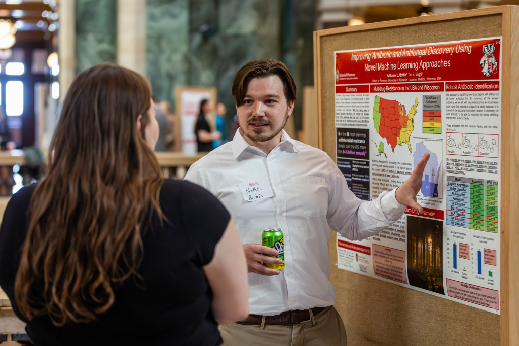 A man talks and gestures to a poster board.