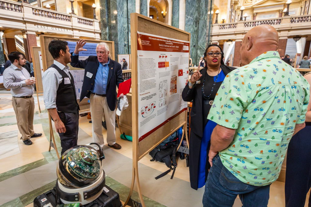 Two groups of people talk in front of poster boards.