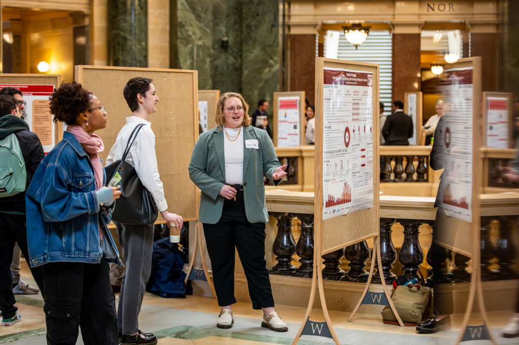 A person talks to another person in front of a poster board.