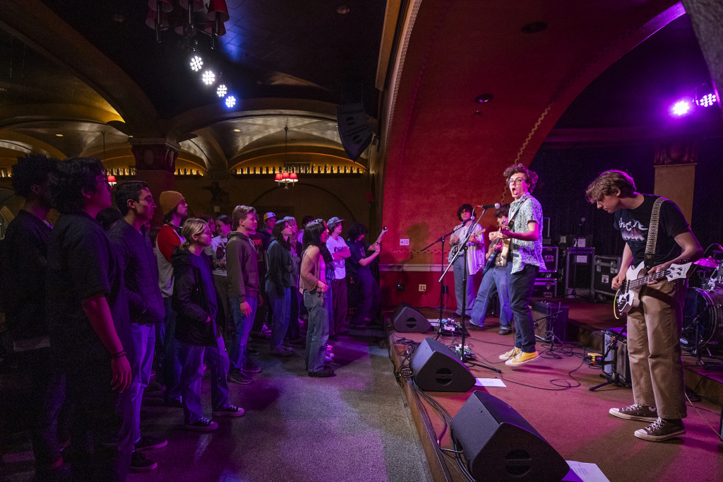 A band plays on a stage while students listen in the audience.