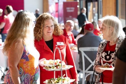 UW Chancellor Jennifer Mnookin stands and smiles as she talks with UW alumni around a table.