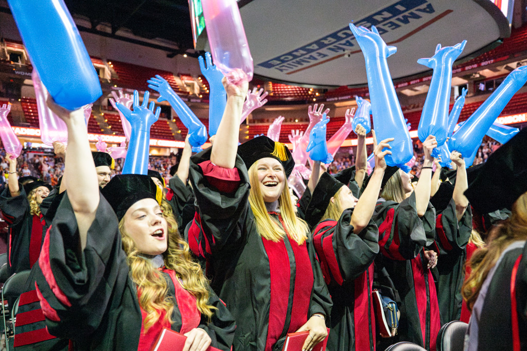 A group of people in graduation robes cheer.