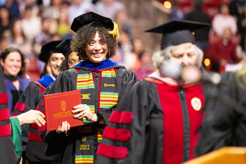 A woman holds a red degree holder and walks.