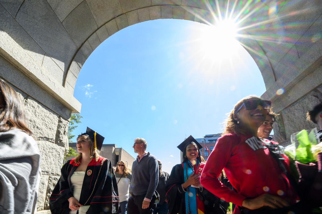 People in commencement robes walk under a stone arch.