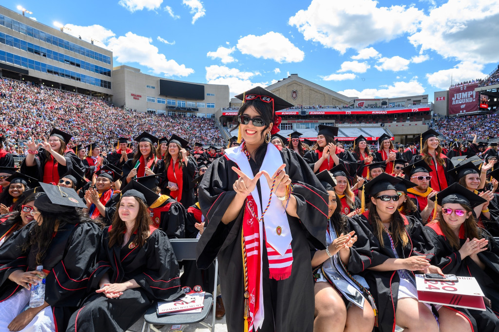 A woman in commencement garb stands and smiles at the camera