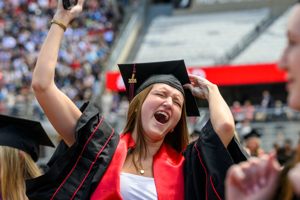 A woman raises her diploma and shouts with joy.