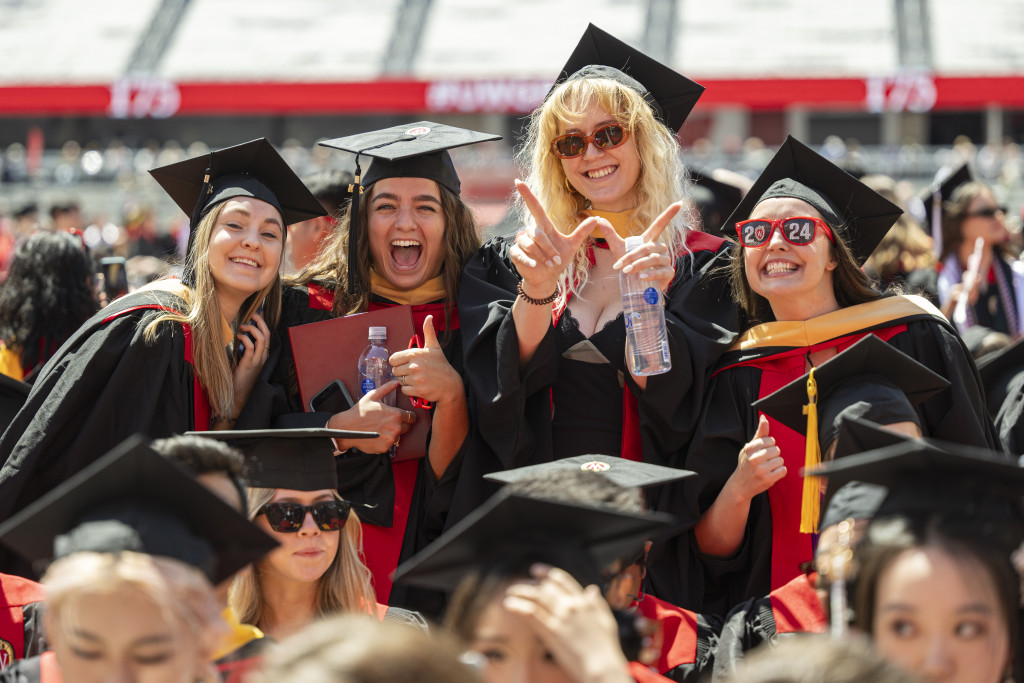 A group of people in graduation gowns stand and smile.