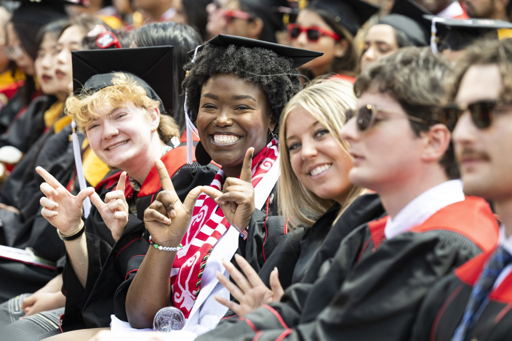 Students in graduation robes smile and make the W signal with their hands.