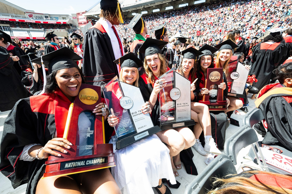 Women in commencement garb display trophies.