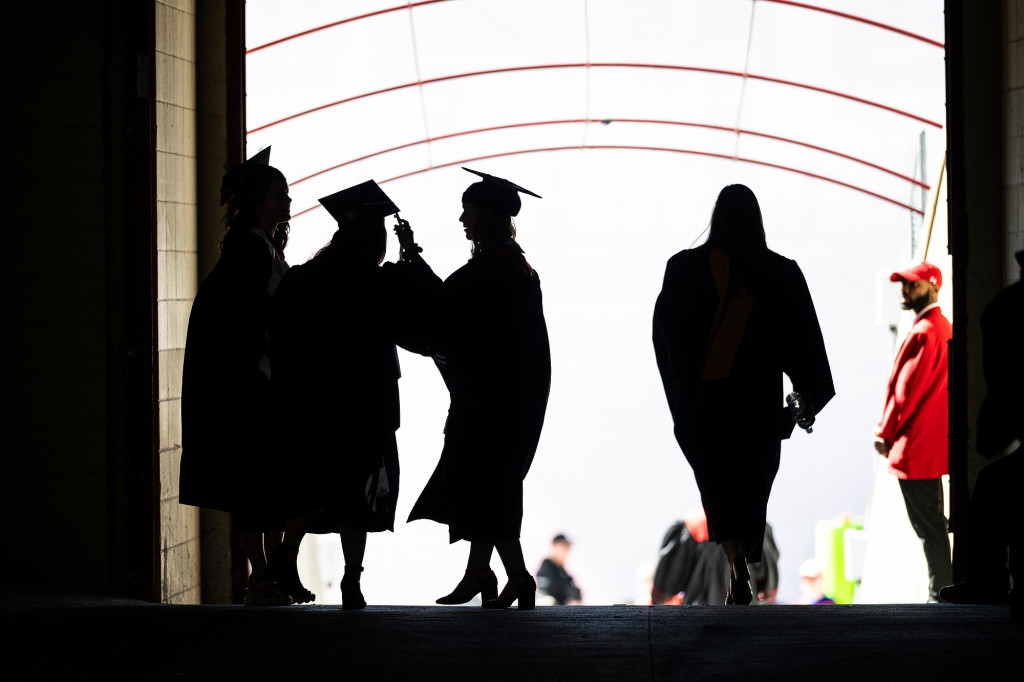 People wearing robes and mortarboard hats are seen in silhouette.