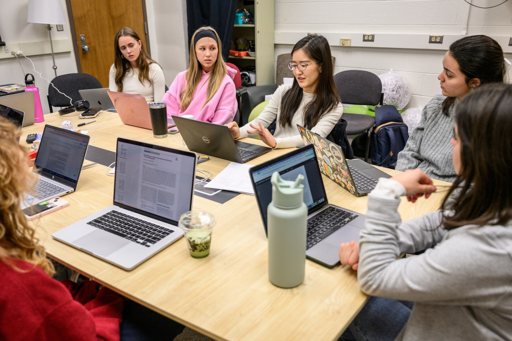 A group of people sit around a table, laptops in front of them, talking.