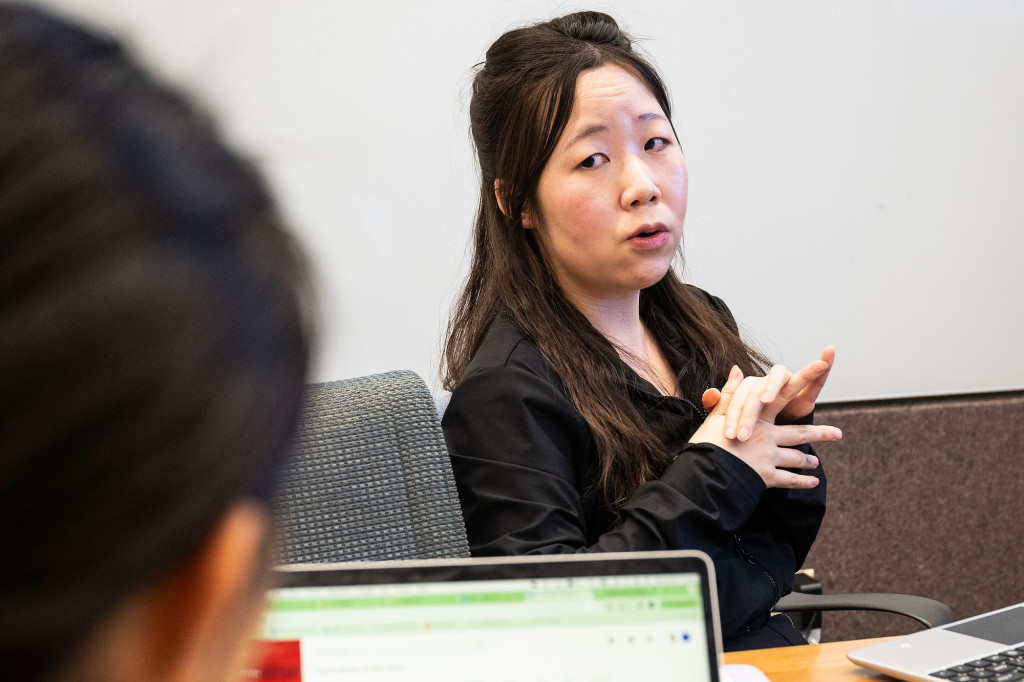 A woman sitting in a chair talks and gestures to two other people.