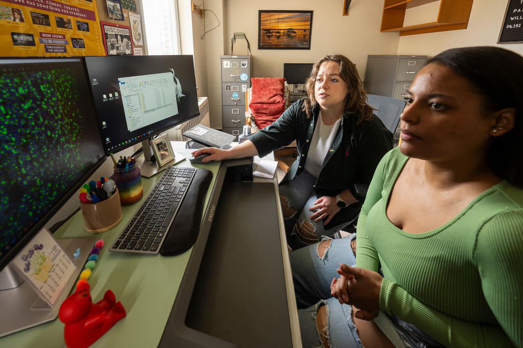 Two women talk in an office, with a computer in front of them.