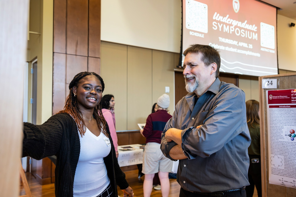 A man and a woman smile and talk, standing in a presentation hall.