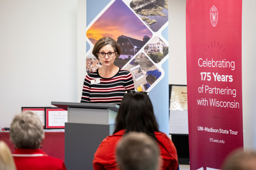 Sarah Schutt stands at a podium surrounded by UW 175 banners and speaks to a seated crowd.